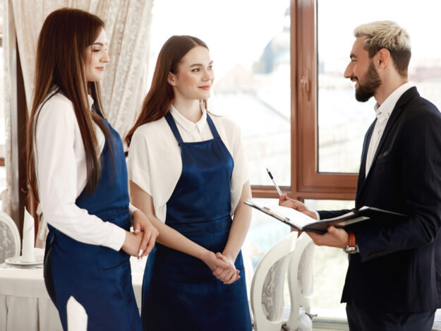 Handsome restaurant manager is talking to waitresses about work Handsome restaurant manager is talking to waitresses about work process
